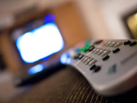 Control remoto de televisor en primer plano, con la pantalla encendida de fondo